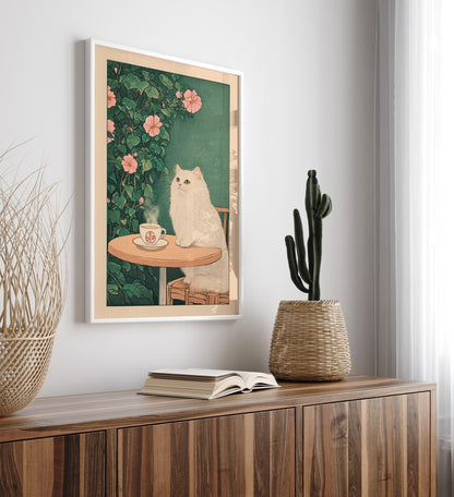 Framed artwork of a white cat by a table with a cup, placed on a wooden surface.